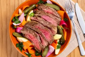 Prato de carne bovina fatiada com legumes assados, demonstrando informativo de ferro heme