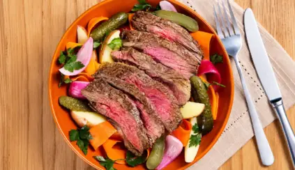 Prato de carne bovina fatiada com legumes assados, demonstrando informativo de ferro heme