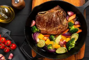 Bife suculento sendo preparado em frigideira com legumes variados. Lembrando que a carne bovina é uma fonte de zinco