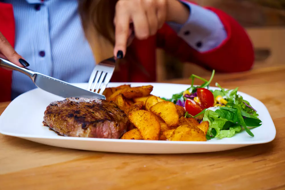 Person cutting meat from a plate with roasted potatoes, green salad and cherry tomatoes, highlighting the expansion of observational studies in nutrition.