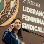 Stephanie Ferreira discursando em evento sobre liderança feminina e sindicalismo rural, ao fundo painel com o logo da iniciativa.