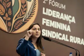 Stephanie Ferreira discursando em evento sobre liderança feminina e sindicalismo rural, ao fundo painel com o logo da iniciativa.