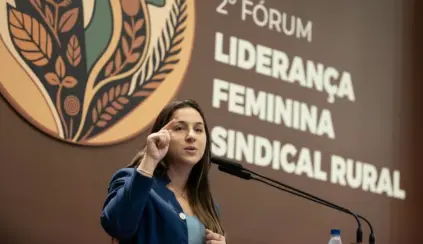 Stephanie Ferreira discursando em evento sobre liderança feminina e sindicalismo rural, ao fundo painel com o logo da iniciativa.