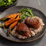 Prato com dois medalhões de carne vermelha ao ponto, acompanhados de legumes assados e molho cremoso