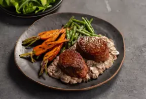 Prato com dois medalhões de carne vermelha ao ponto, acompanhados de legumes assados e molho cremoso