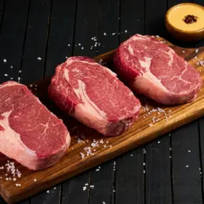 Três pedaços de carne bovina fresca, cortadas em filé, apresentados sobre uma tábua de madeira, ideal para aprender como conservar carnes de forma correta.