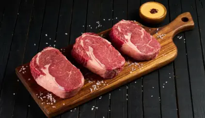 Três pedaços de carne bovina fresca, cortadas em filé, apresentados sobre uma tábua de madeira, ideal para aprender como conservar carnes de forma correta.