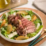 Salada com carne vermelha cozida e cortada em fatias, acompanhada de folhas verdes, fatias de laranja e queijo