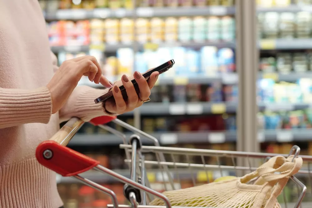 Pessoa usando celular em supermercado com carrinho de compras, destacando a busca por nova carne premium