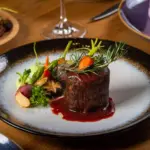 Deliciosa carne premium apresentada com molho, acompanhada de legumes e vegetais frescos em um prato sofisticado