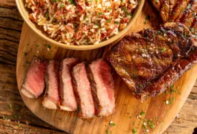 Cortes de chorizo ao ponto para malpassado servidos sobre tábua de madeira com guarnição de arroz com carne seca desfiada
