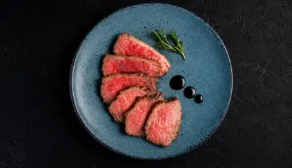Plato con carne fatiada servida em prato azul com ervas frescas e pingos de molho, em fundo escuro, criando uma experiência do consumidor com apresentação gourmet.