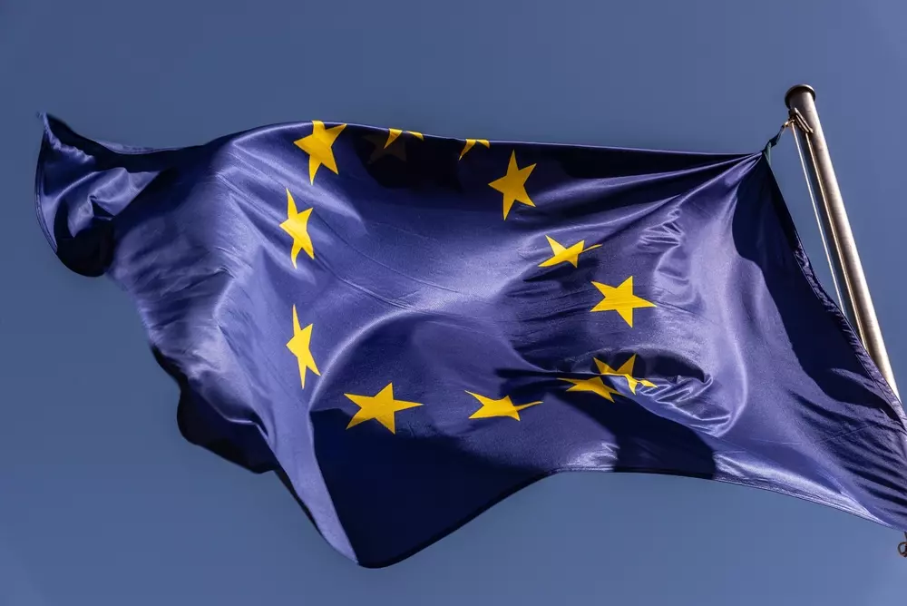 Bandeira da União Europeia hasteada ao vento, com fundo azul e estrelas douradas em círculo