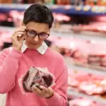 Mulher analisando uma peça de carne no supermercado, destacando a importância da rotulagem internacional