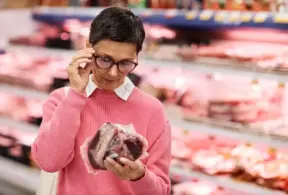 Mulher analisando uma peça de carne no supermercado, destacando a importância da rotulagem internacional