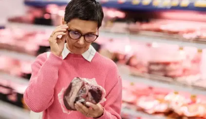 Mulher analisando uma peça de carne no supermercado, destacando a importância da rotulagem internacional