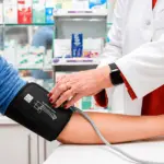 Médica verifica a pressão arterial em paciente com aparelho de pressão no braço, em ambiente clínico, tema relacionado a pressão alta e cuidados com a saúde.