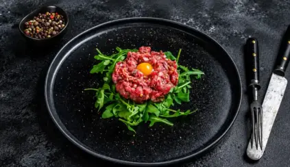 Carne crua em forma de tartare no centro do prato, com gema de ovo e folhas de rúcula