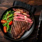 Carne mal passada em uma frigideira: bife grelhado com interior rosado, acompanhado de folhas verdes e tomates-cereja no prato