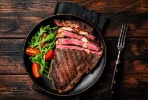 Carne mal passada em uma frigideira: bife grelhado com interior rosado, acompanhado de folhas verdes e tomates-cereja no prato