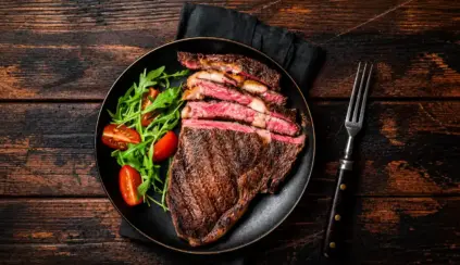 Carne mal passada em uma frigideira: bife grelhado com interior rosado, acompanhado de folhas verdes e tomates-cereja no prato
