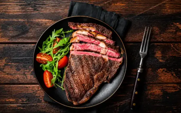 Carne mal passada em uma frigideira: bife grelhado com interior rosado, acompanhado de folhas verdes e tomates-cereja no prato