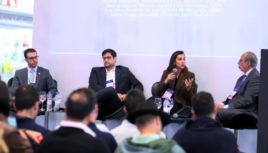 Painel em evento do setor de carnes com participantes sentados, palestrando em contexto de tendências do mercado da carne. Audiência ao fundo.