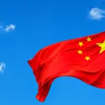Bandeira da China com estrelas amarelas ao vento, haste vermelha com brasão dourado, em referência às novas diretrizes alimentares da China.