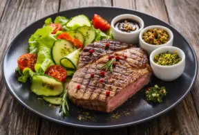 Prato com bife grelhado e salada de folhas, tomate e pepino, acompanhado de molhos em tigelas. Zinco da carne x zinco vegetal em refeição nutritiva com carne e vegetais