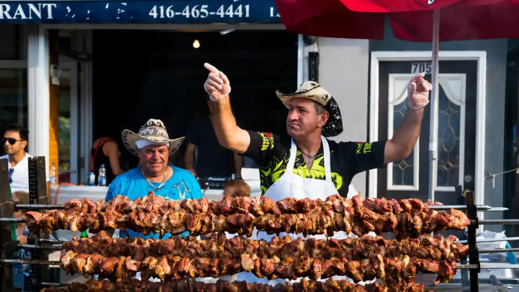 Churrasco de verão no Canadá: cozinheiro com chapéu e avental assando espetinhos no espeto, grelhados ao ar livre em feira multicultural