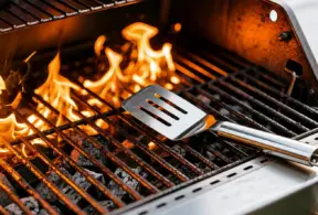 churrasco: grelha de churrasqueira acesa com chamas laranjas e uma espátula sobre as barras do grill, preparando carne para assar