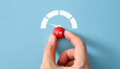Mão segurando uma bolinha vermelha com o símbolo Fe e indicador de velocidade em forma de semicírculo, representando ferro heme e o controle de níveis de ferro no organismo.