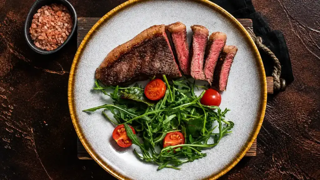 Prato com cortes de carne e salada verde com tomate, sugerindo proteína para recuperação muscular pós-treino.
