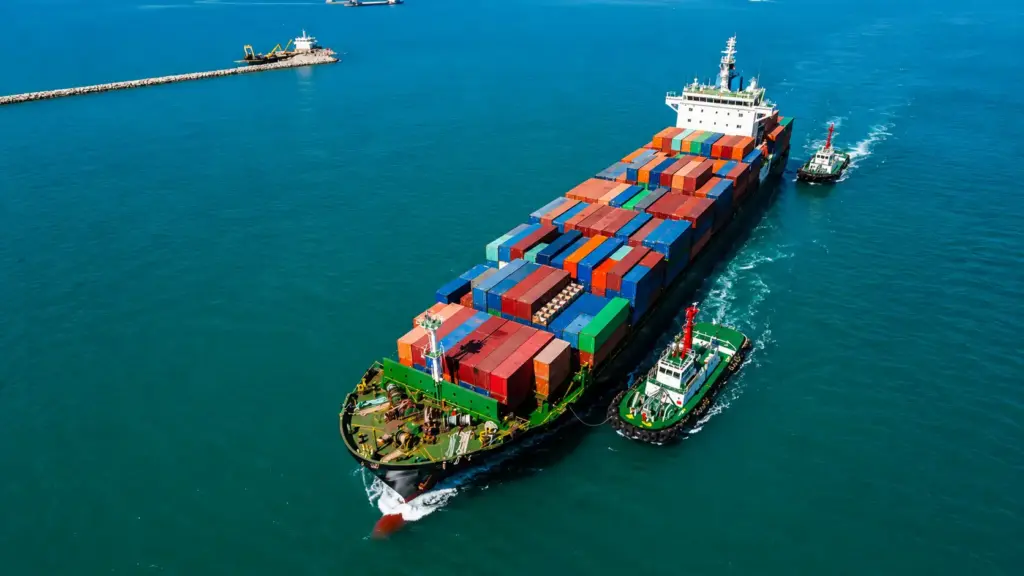 segurança alimentar: Vista aérea de um navio cargueiro com contêineres coloridos navegando no mar, ao lado de um rebocador, com água azul ao fundo. Foto aérea do transporte marítimo.