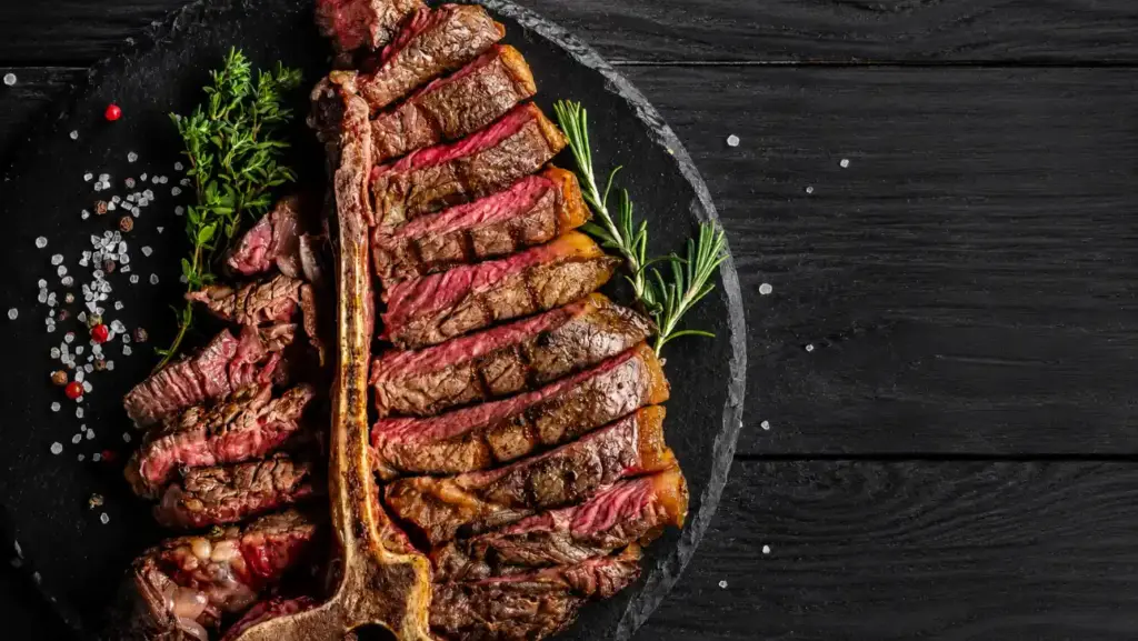 nomes diferentes de carne: Bife Porterhouse e T-bone com cortes de carne assados na frigideira de pedra, temperados com ervas e pimenta sobre mesa escura.