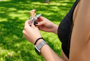 Pessoa ao ar livre segurando uma barrinha energética durante atividade física, opção prática de alimentação esportiva