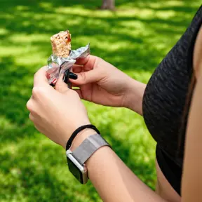 Pessoa ao ar livre segurando uma barrinha energética durante atividade física, opção prática de alimentação esportiva