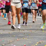 Um grupo de corredores, com números de inscrição bem visíveis, corre por uma rua coberta de confete colorido durante uma corrida de rua ou maratona. Apenas suas pernas e pés estão visíveis, demonstrando a dedicação e a energia alimentadas pela proteína para corredores.