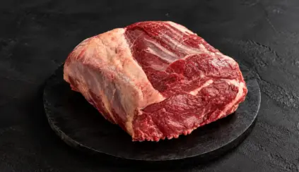 Peça de carne bovina crua em corte com gordura aparente sobre uma base preta de pedra, pronta para preparo culinário; carne de segunda em destaque.