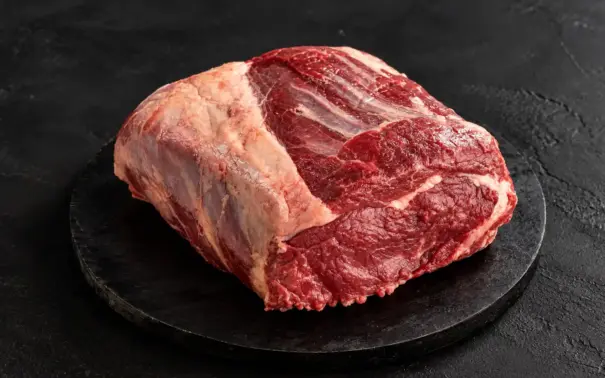 Peça de carne bovina crua em corte com gordura aparente sobre uma base preta de pedra, pronta para preparo culinário; carne de segunda em destaque.