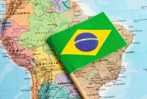 Bandeira do Brasil sobre mapa da América do Sul, com estados e países ao fundo; referência para tema de CBAM e carne brasileira.