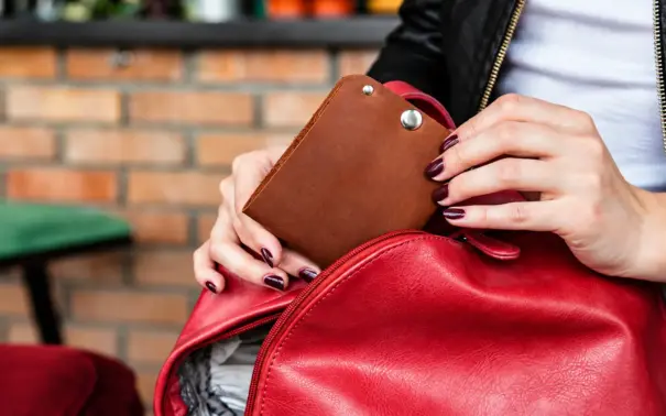 Mulher segura uma bolsa vermelha com uma carteira marrom acoplada, em ambiente externo com parede de tijolos ao fundo. dia nacional da pecuária