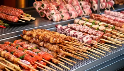 Churrasco na China com espetinhos grelhados em uma chapa industrial, com legumes e ervas na composição dos pratos.
