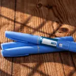 Duas canetas emagrecedoras azuis com a indicação de 1 mg apoiadas sobre uma superfície de madeira.