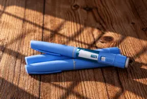 Duas canetas emagrecedoras azuis com a indicação de 1 mg apoiadas sobre uma superfície de madeira.